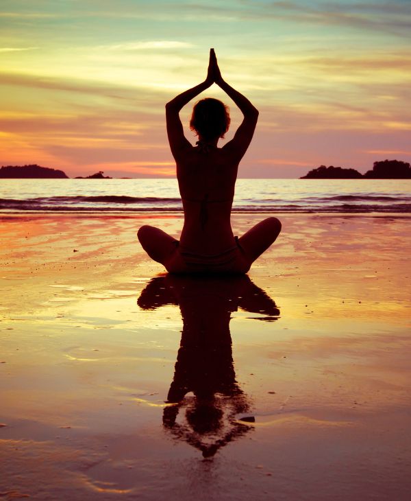 Mujer haciendo yoga frente al mar en el atardecer